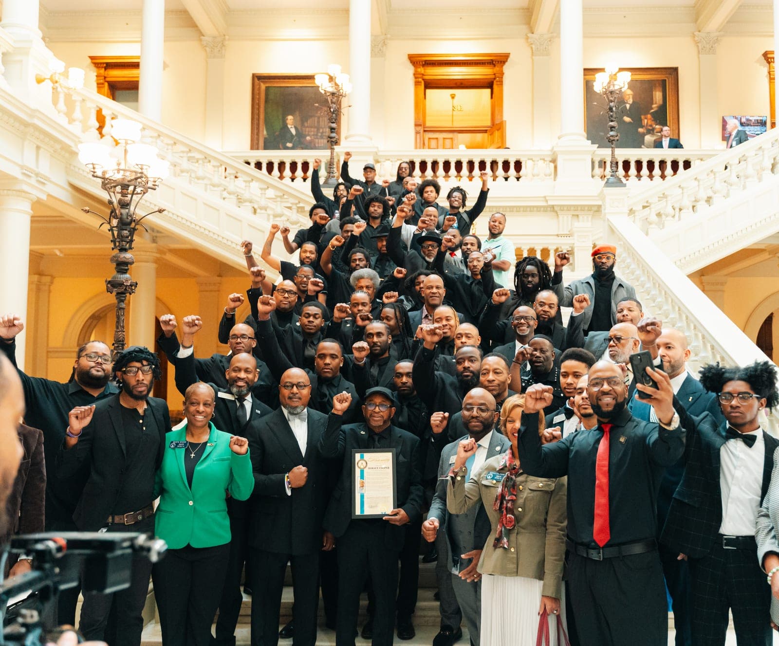 Black Male Initiative Fund members gather on the steps inside a state capitol, many raising their fists.