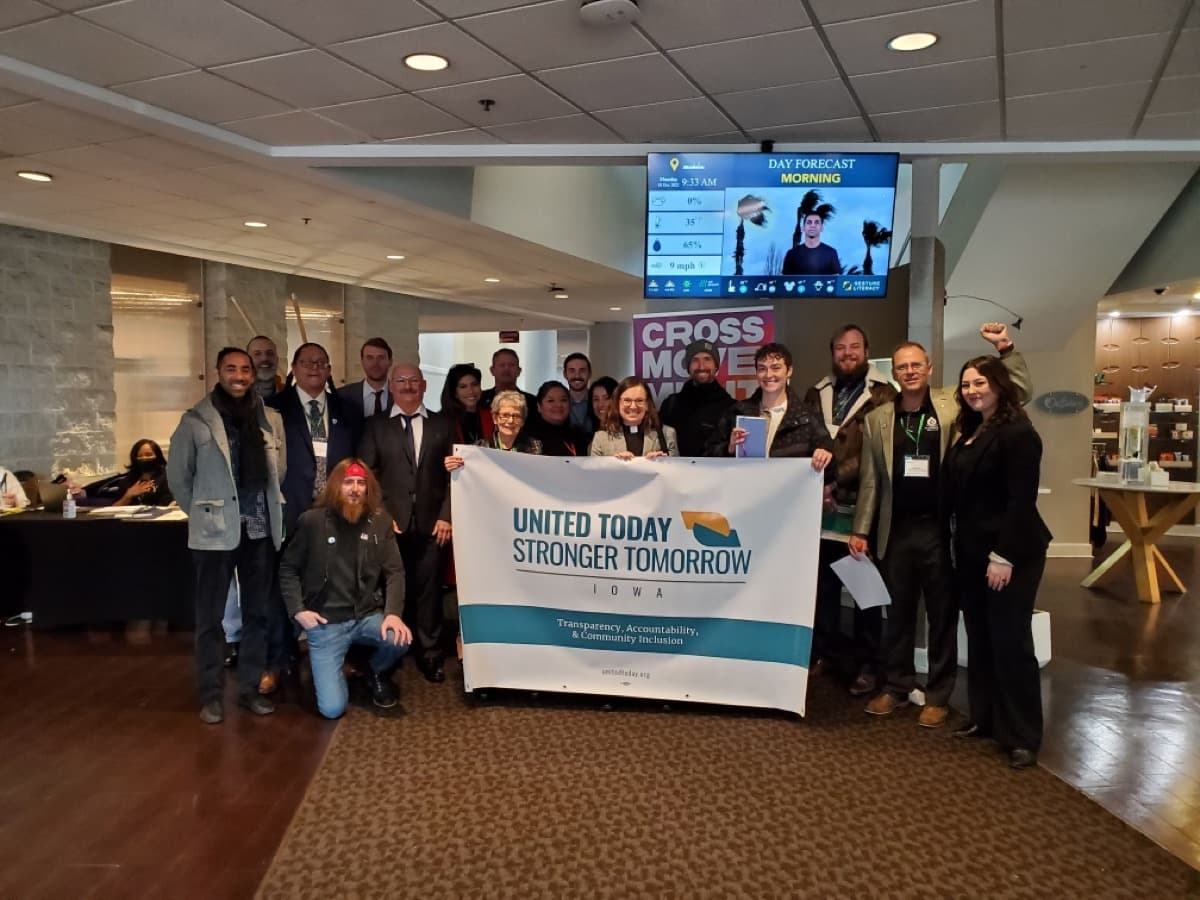 About 25 people stand behind a United Today, Stronger Tomorrow Iowa banner.