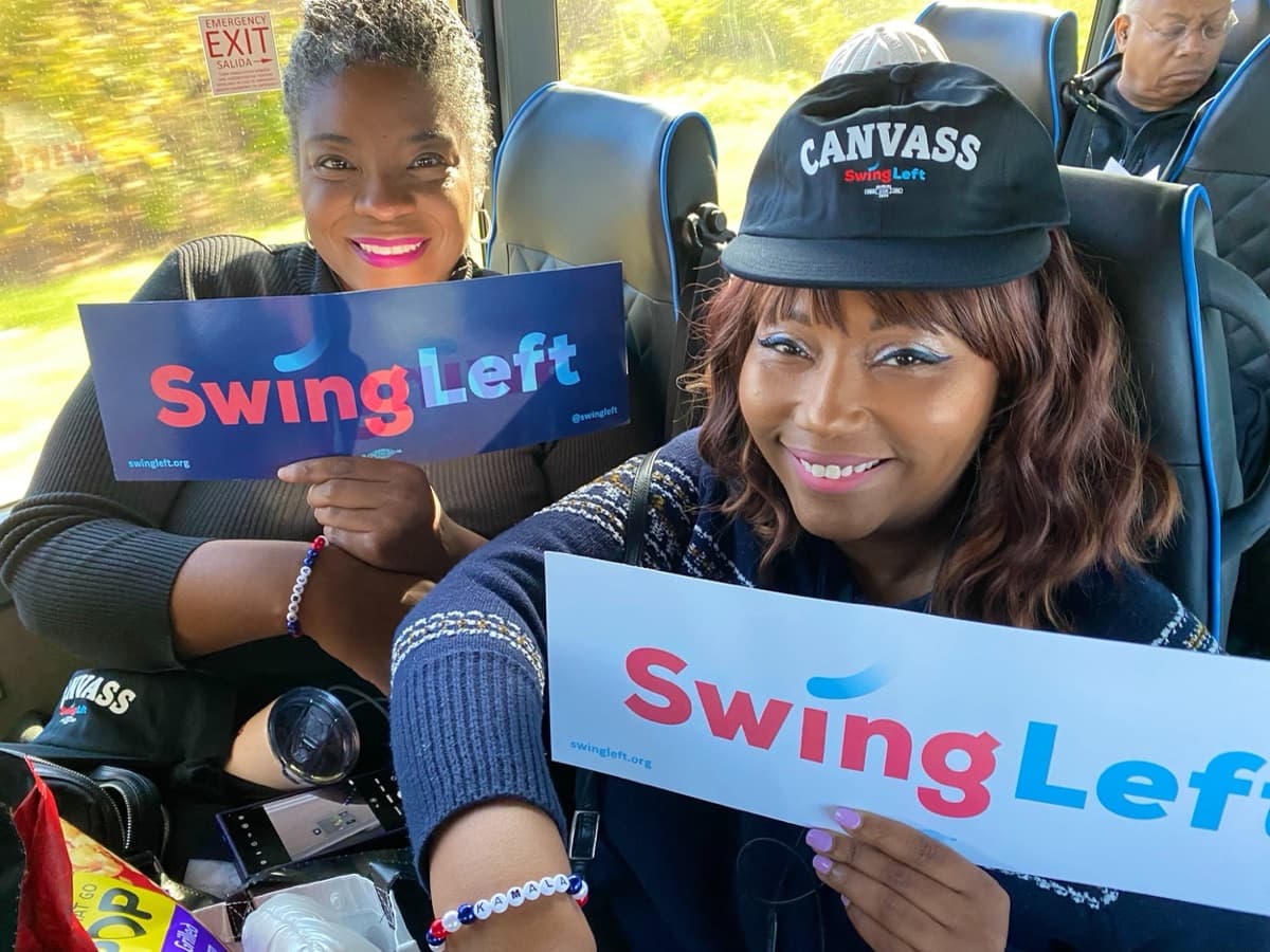 Two Swing Left volunteers hold Swing Left signs on a canvass bus.