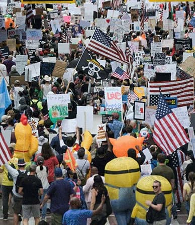 A packed No Kings march fills a street, with American flags and handmade signs held high.