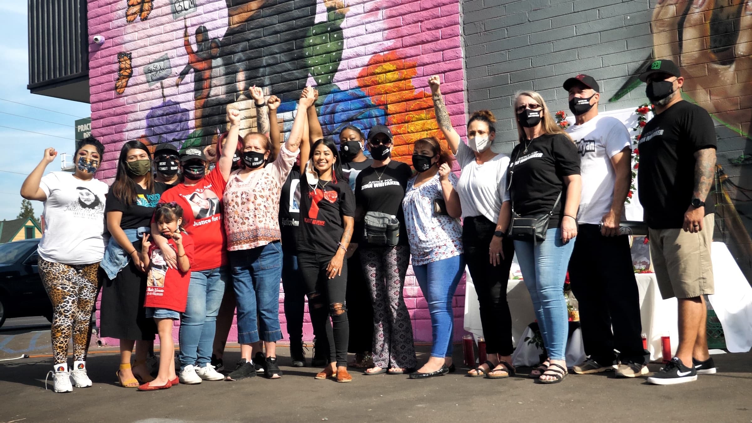 Poder in Action members, some with children, raise their fists in front of a colorful mural in Phoenix
