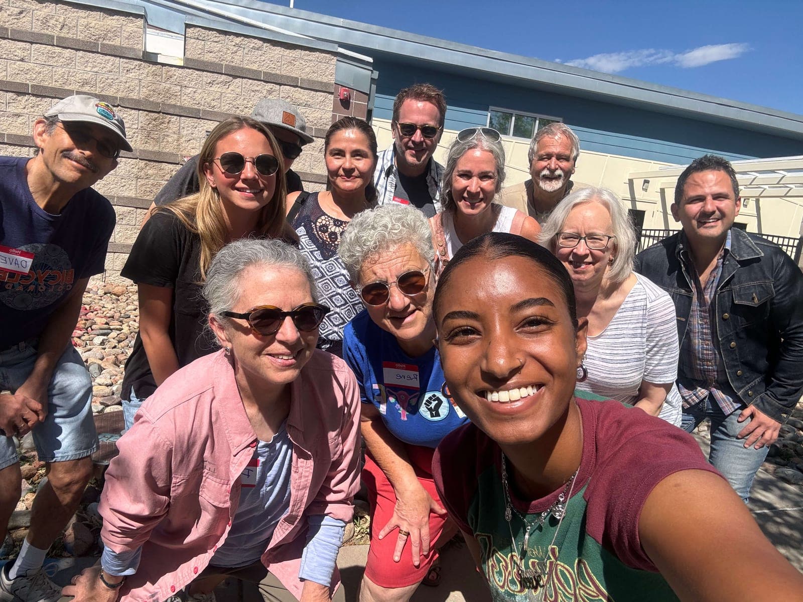 Trust Brigade volunteers crowd into a sunny group selfie outdoors.