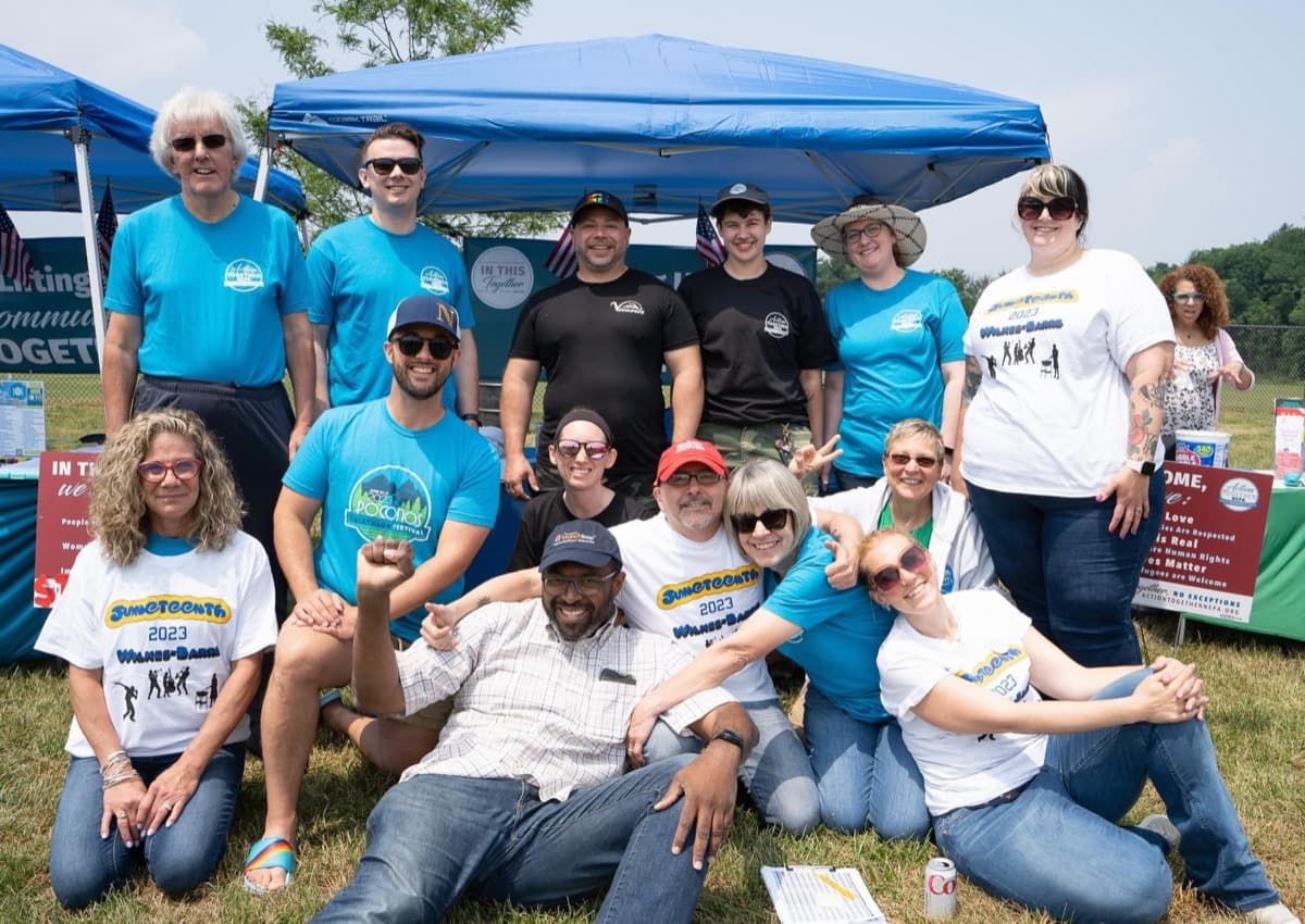 About 15 Action Together NEPA members in matching shirts pose under a tent at an outdoor event.