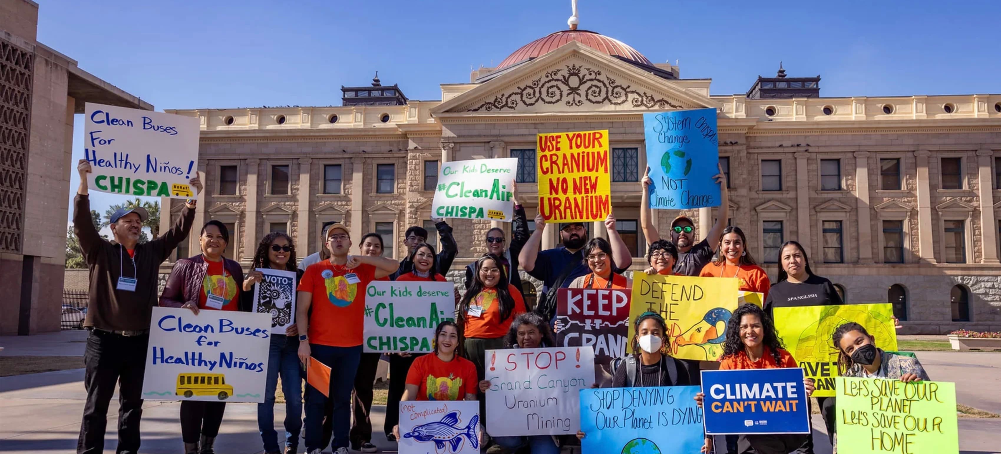 Chispa Arizona members hold clean air and climate signs in front of the Arizona State Capitol.