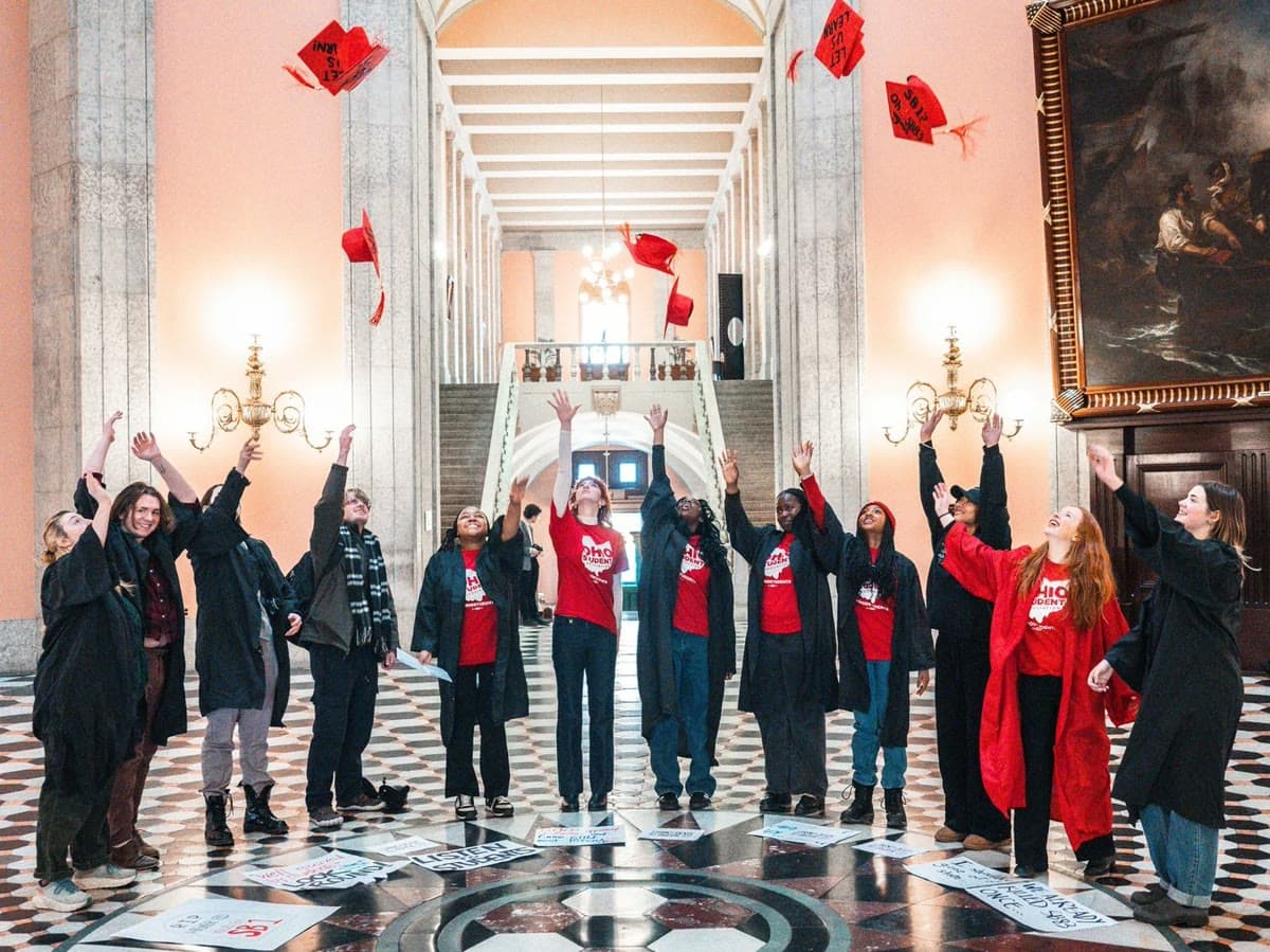 Ohio Student Association members in red shirts and graduation gowns toss red caps in the air under a statehouse rotunda.
