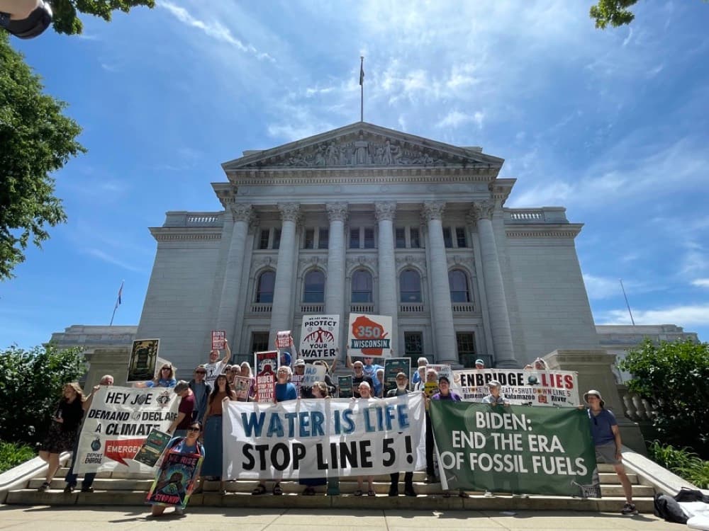 Members of 350 Wisconsin Action hold banners reading “Water is life, stop Line 5” on the steps of the Wisconsin Capitol.
