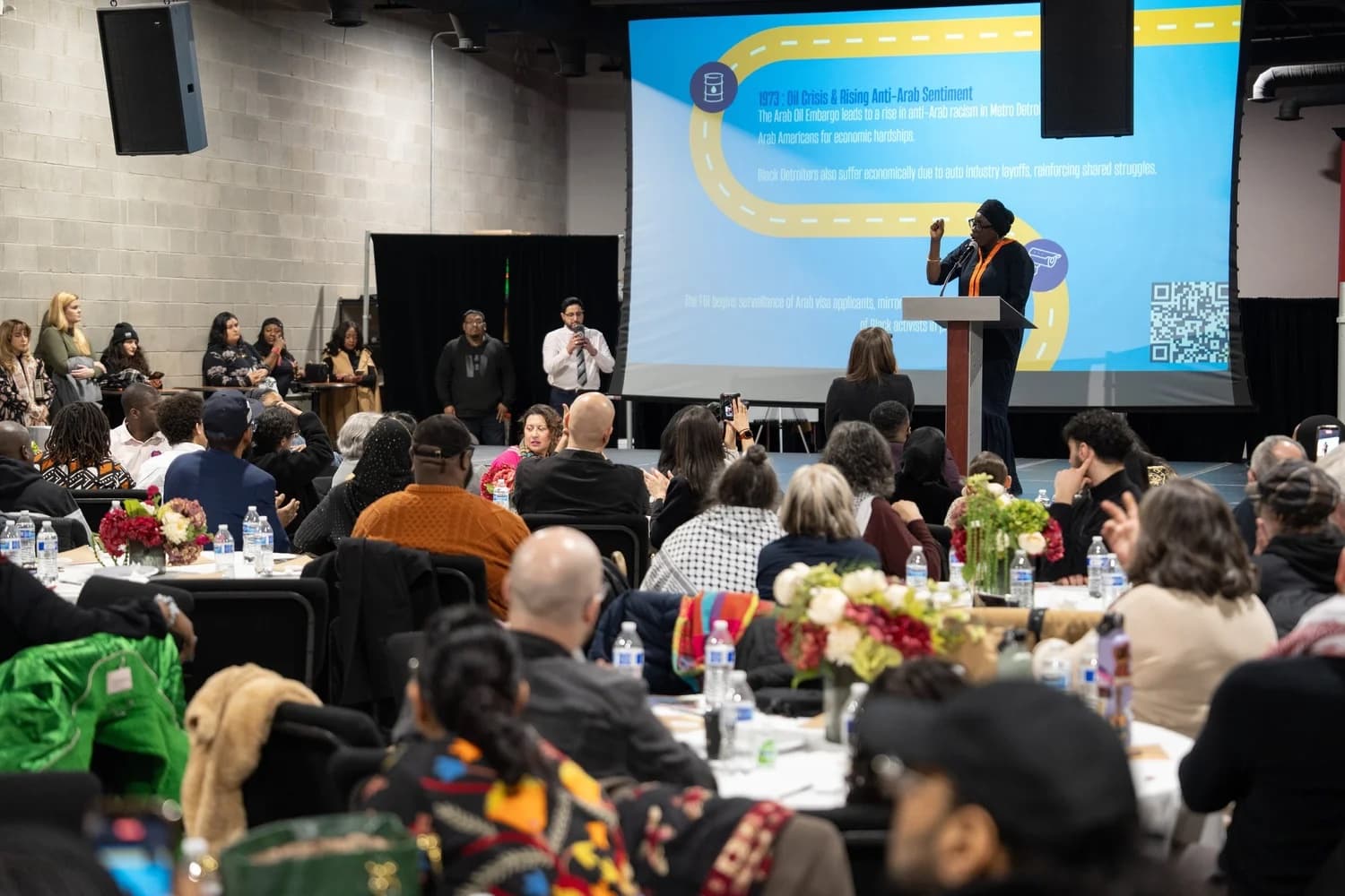 Guests at round tables listen to a speaker at a Black and Arab solidarity iftar.