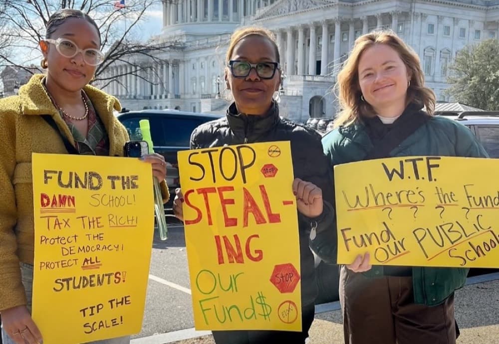 Three Popular Democracy in Action members hold signs at a rally to protect school funding.
