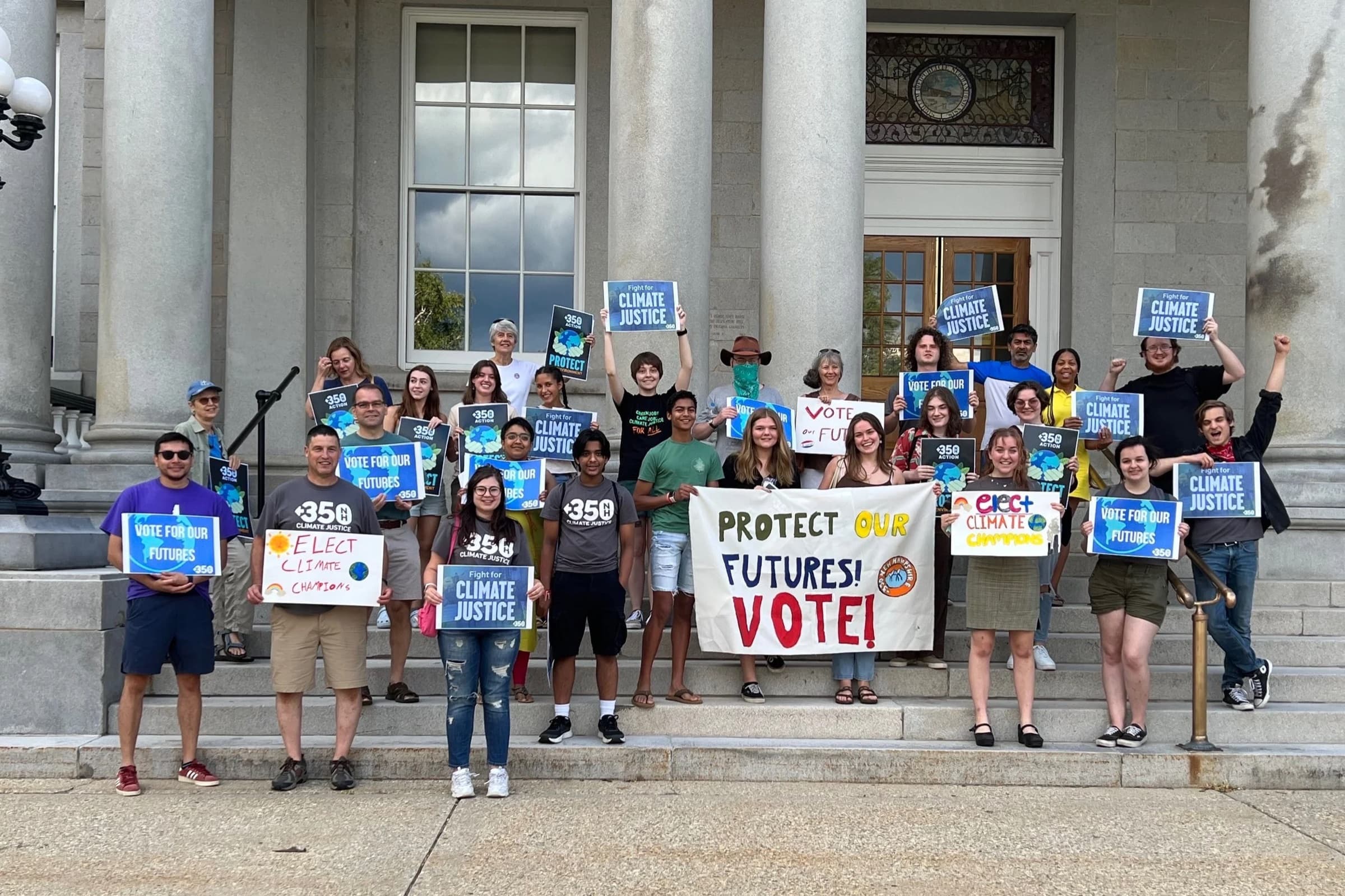 350NH Action volunteers with 350 and climate signs and a ‘Protect Our Futures! Vote!’ banner on the steps of a New Hampshire public building