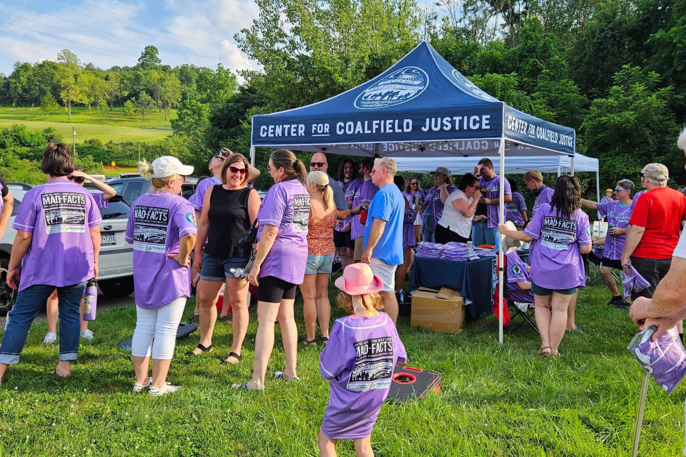 A crowd in purple shirts gathers at the Center for Coalfield Justice tent at a community event in southwestern Pennsylvania