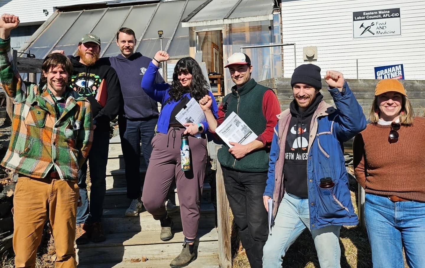 Food AND Medicine organizers raise their fists in front of a Maine building.
