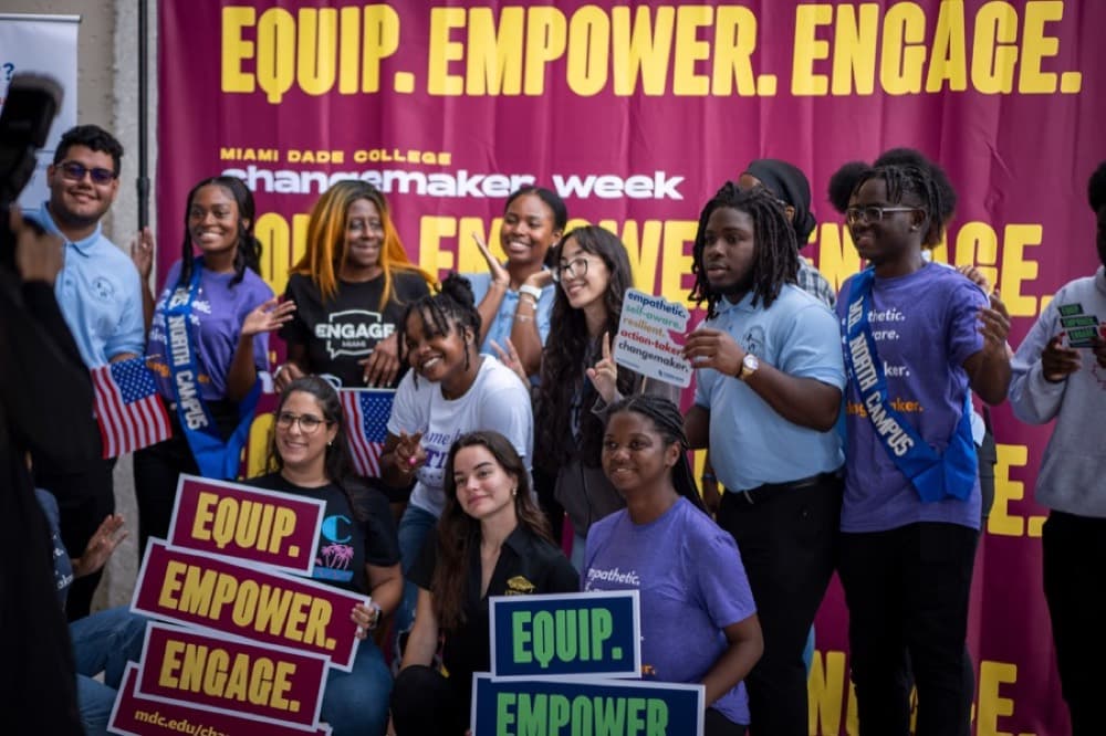 Young Engage Miami volunteers smile in front of an Equip, Empower, Engage banner.