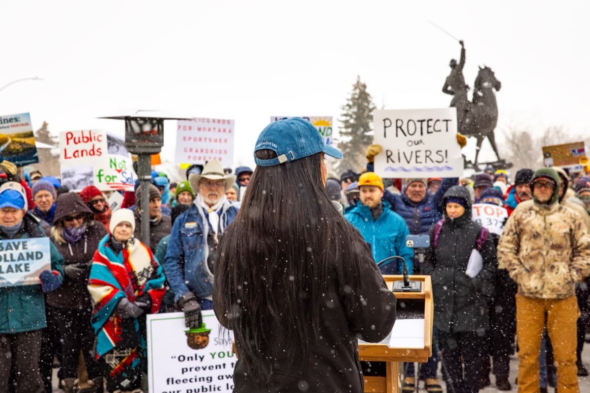 A large crowd with signs, including “Protect our rivers!”, rallies for public lands in the snow.