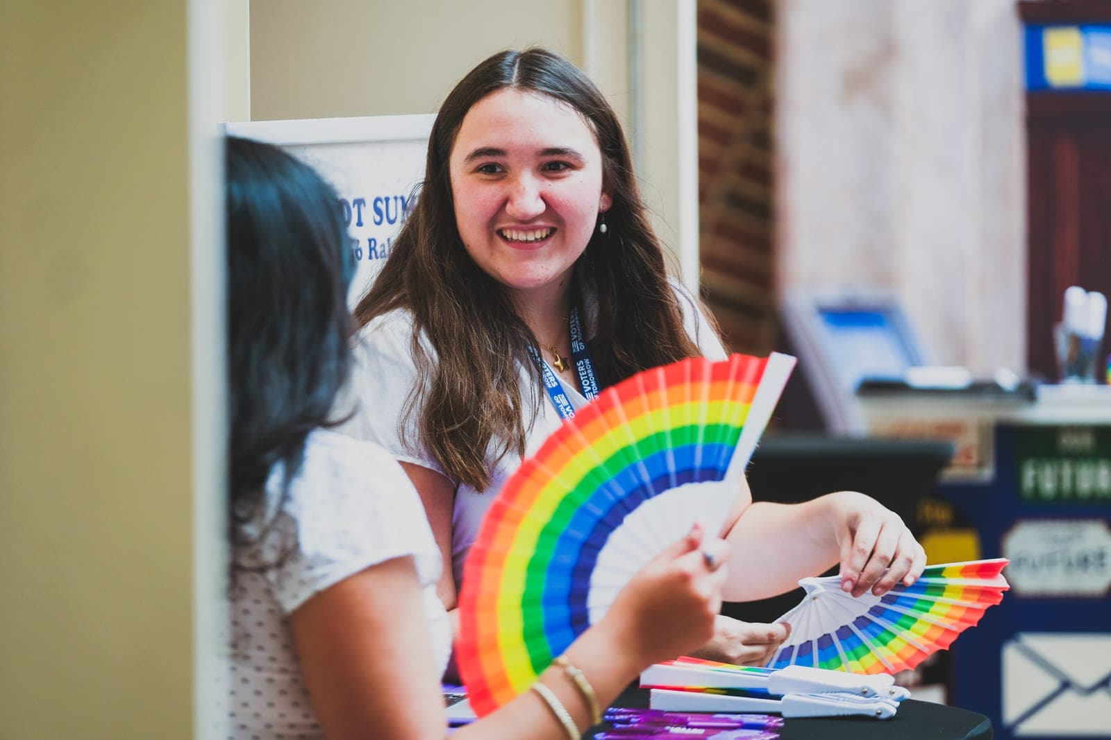 An OutVote organizer smiles while handing out rainbow fans at a table.