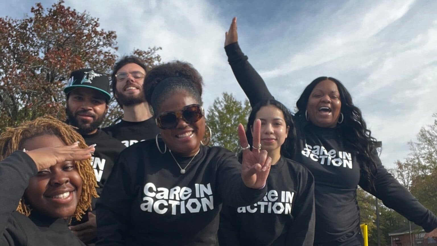 Care in Action members in black Care in Action shirts smile and raise their hands together.