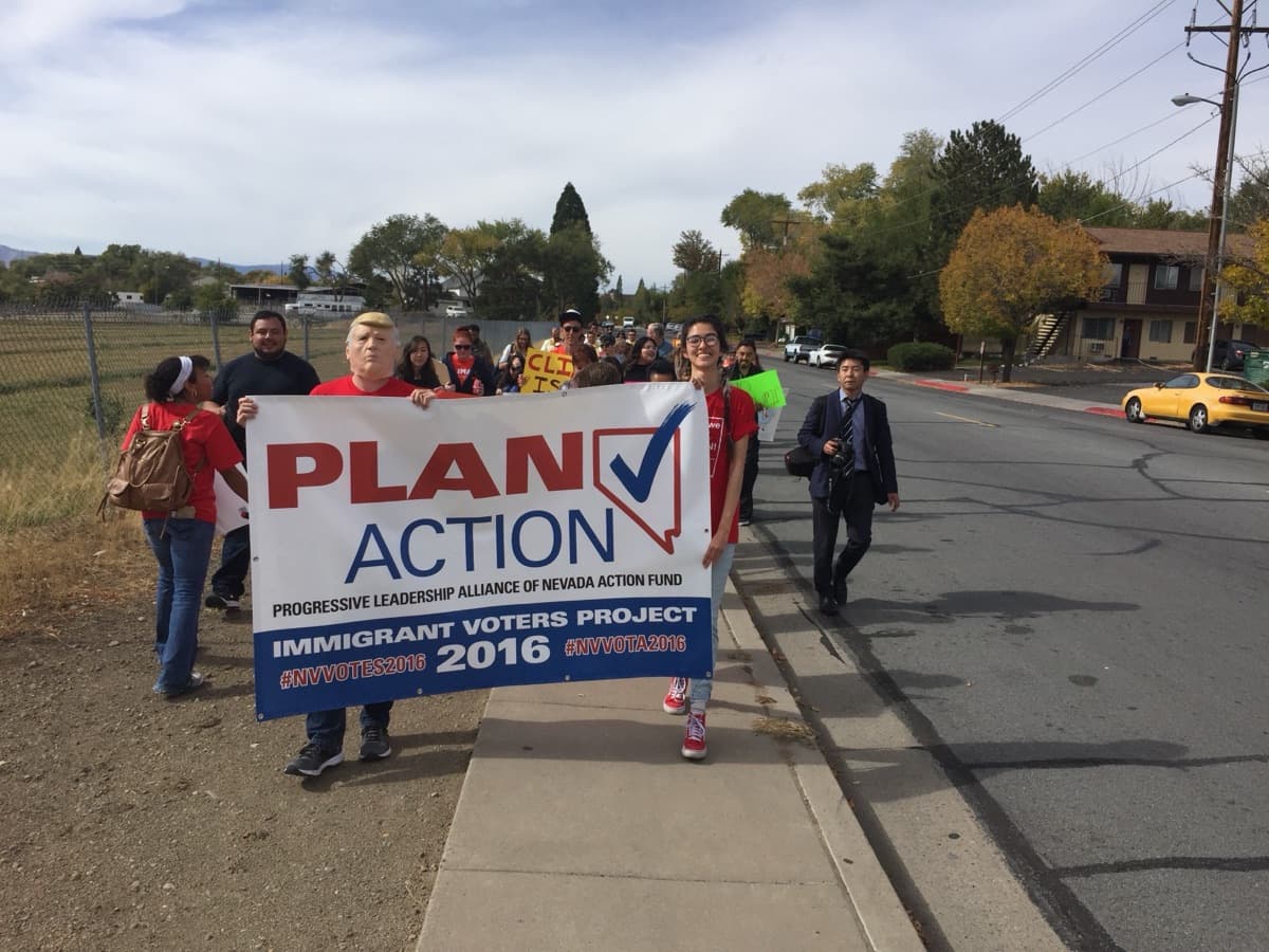 Marchers carry a PLAN Action Immigrant Voters Project banner down a street.