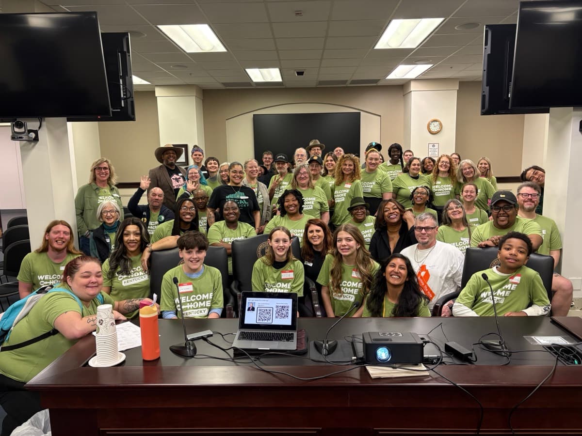 A large group in green shirts fills a meeting room at a Common Ground Kentucky gathering.