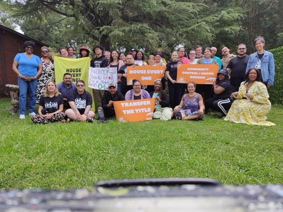 Fuerte Arts Movement members and allies sit and stand together on a lawn at a housing rally.