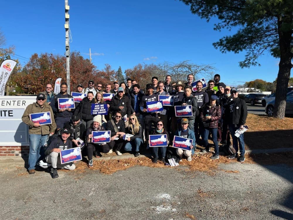 A large group of Battleground New York volunteers pose outdoors holding Battleground New York signs.