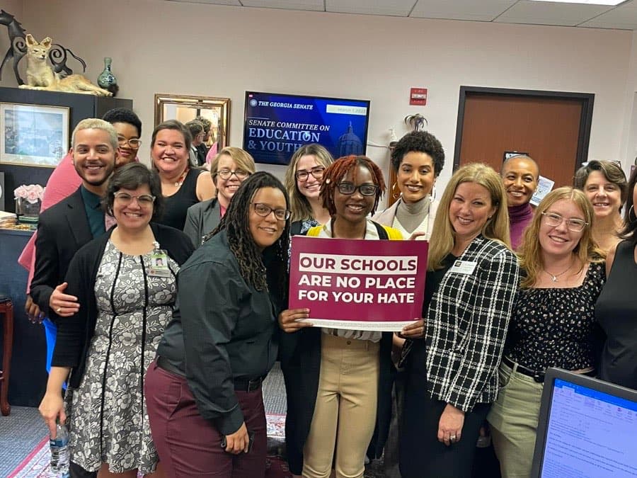Georgia Equality staff and allies pose with a sign reading “Our schools are no place for your hate” at the Georgia Capitol.