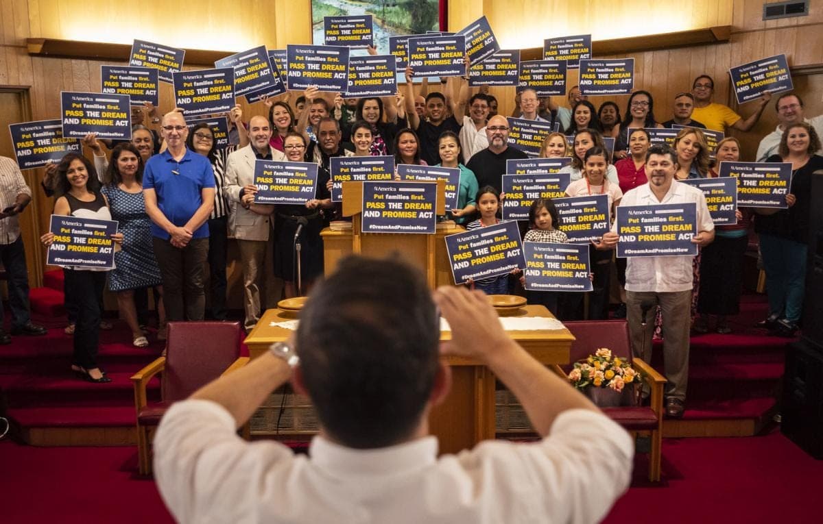 A packed room of NC Latino Power supporters holds up signs at a gathering.