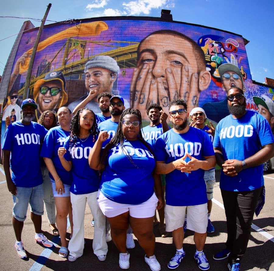 A group of 1Hood Power organizers in blue shirts pose together in front of a mural.