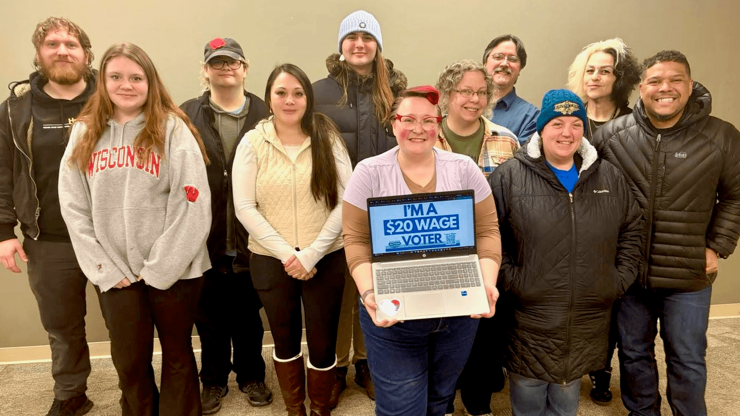Citizen Action of Wisconsin members in Green Bay pose together, one holding a laptop reading “$20 wage voter”.
