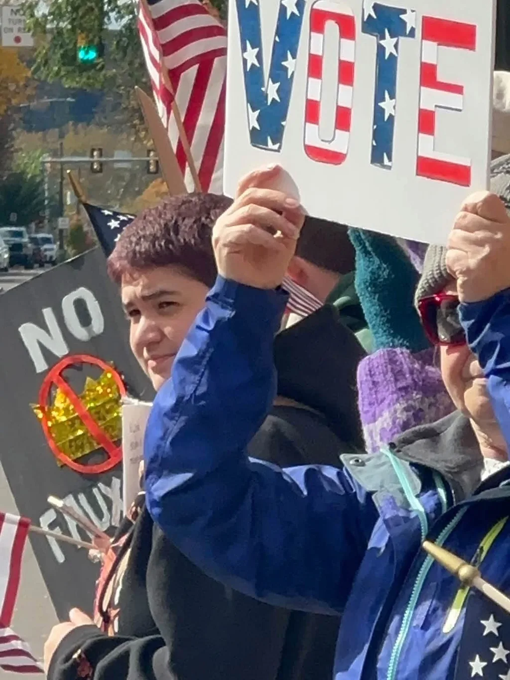 Rally-goers holding a hand-lettered “Vote” sign, a “No Kings” sign and American flags at the silent rally in Bloomsburg.