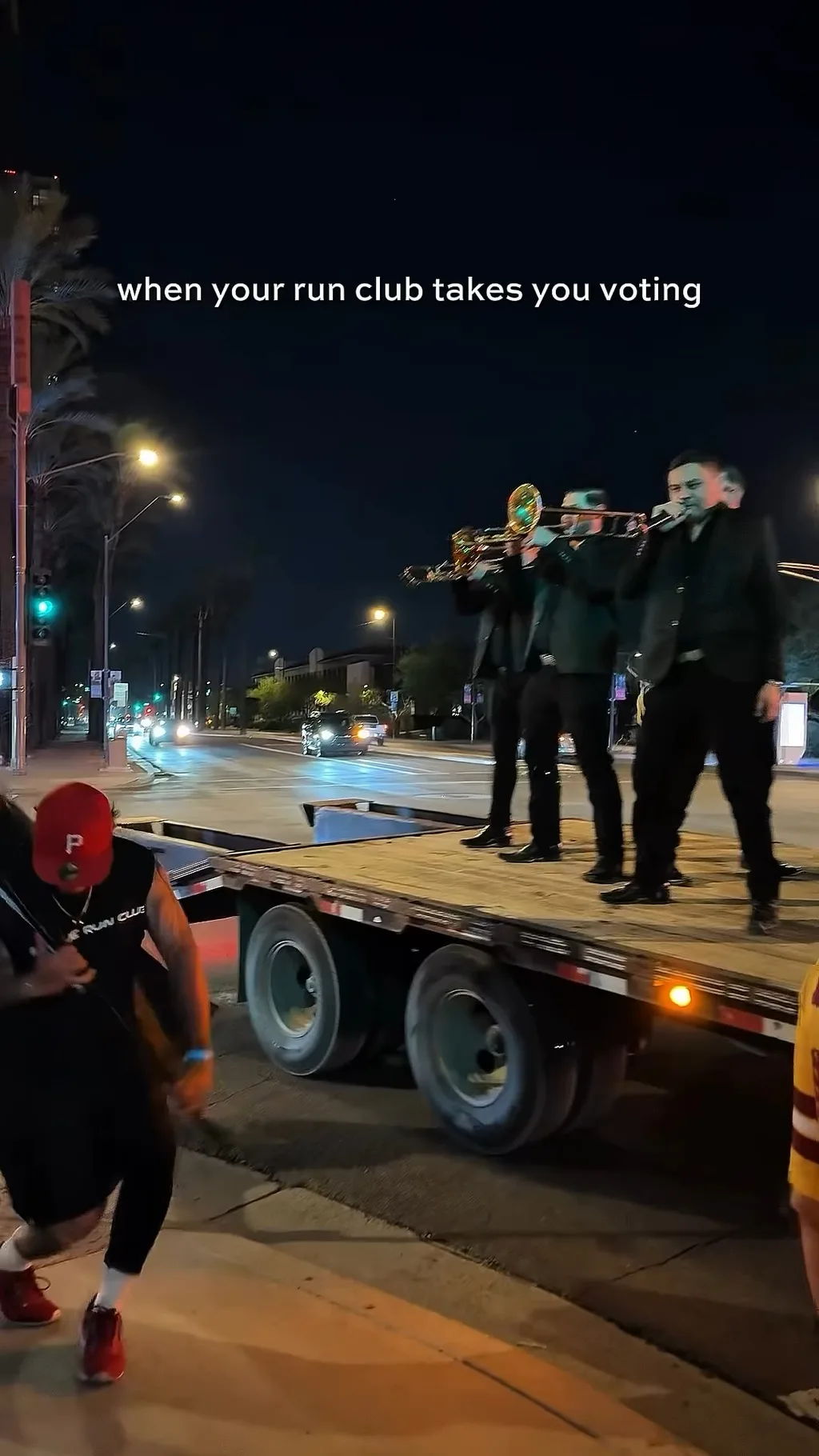 A banda playing brass on a flatbed truck at night in downtown Phoenix as a runner passes, during LUCHA’s Run the Vote.